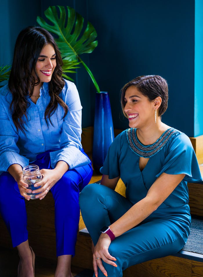 Two women enjoying a lively conversation indoors, showcasing stylish and colorful attire.